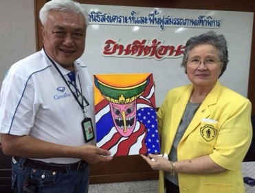 เด็กพิการได้วาดภาพหน้ากากอยู่ระหว่างธงชาติไทยและธงชาติสหรัฐอเมริกา แล้วนำมามอบให้กับคณะโครงการ