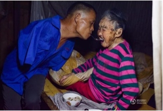 นาย‘เฉิน ซิงหยิน’ วัย 48 ปี พิการแขนด้วนทั้งสองข้างกำลังใช้ปากคาบช้อนป้อนข้าวผู้เป็นแม่