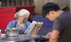 ผู้สูงอายุใช้แว่นขยายส่องอ่านหนังสือพิมพ์