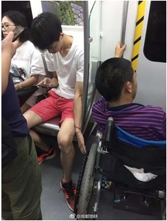 เด็กหนุ่มก้มหน้าเล่นมือถือ แต่อีกมือช่วยจับรถเข็นคนพิการไว้
