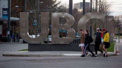 Young men walk past large letters spelling out UBC at the University of British Columbia in Vancouver on November 22, 2015.